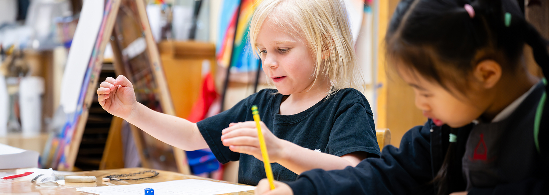 Two junior school students are playing with dice and writing during an instructional exercise.