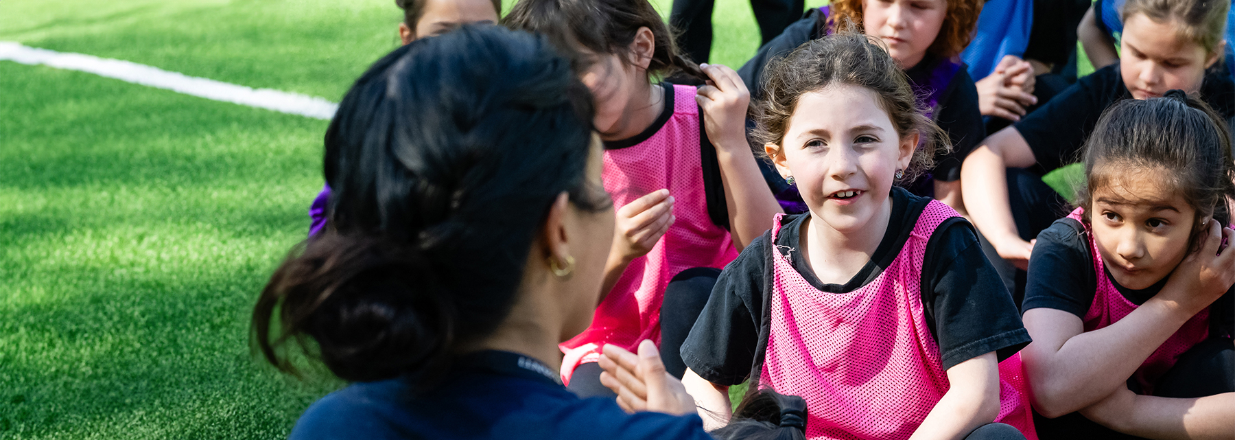 A young BSS student wearing a pink jersey is looking up at her teacher outside.