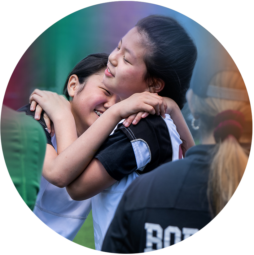 Two BSS middle school students are hugging on the sports field.